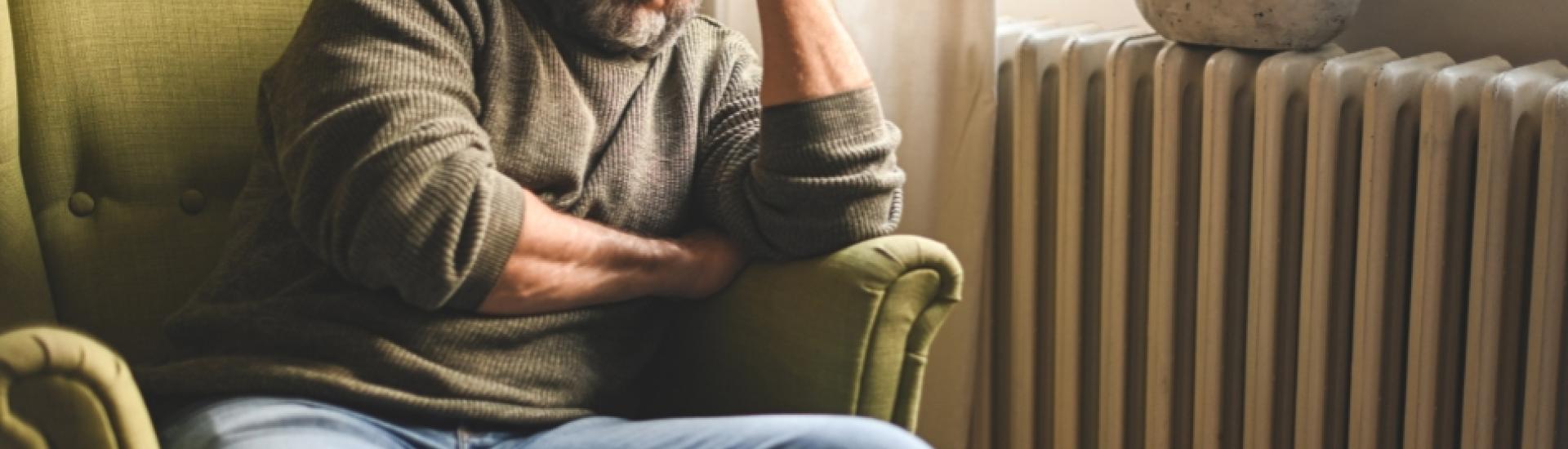 Older man sitting in chair with head in hands looking tired and stressed