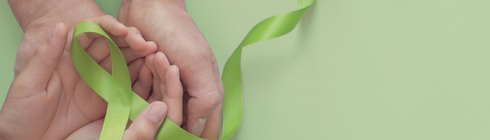Two hands cupped together holding green ribbon in shape of mental health awareness ribbon