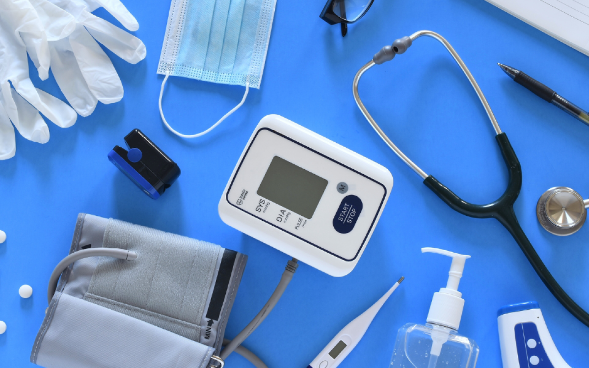 Medical equipment on a table: stethoscope, blood pressure reader, mask, clinical gloves, thermometer