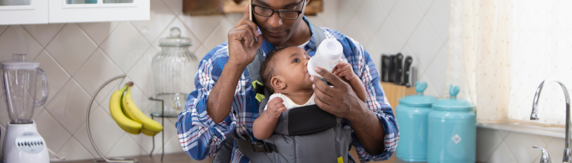 A man bottle feeding his baby whilst sat at a laptop working