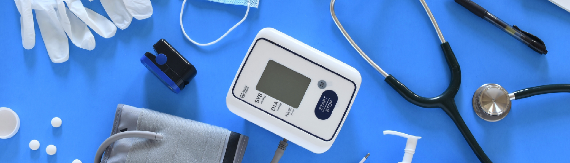 Medical equipment on a table: stethoscope, blood pressure reader, mask, clinical gloves, thermometer