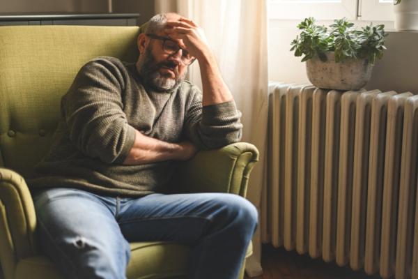 Older man sitting in chair with head in hands looking tired and stressed
