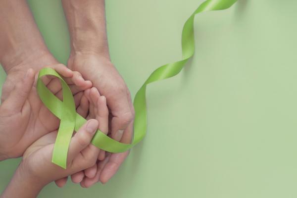 Two hands cupped together holding green ribbon in shape of mental health awareness ribbon
