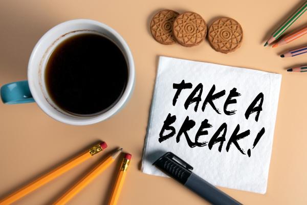 Coffee, pens, biscuits on desk with a note saying 'Take a break!'