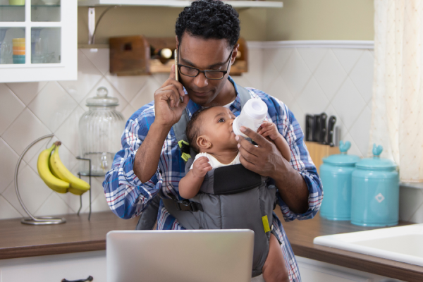 A man bottle feeding his baby whilst sat at a laptop working