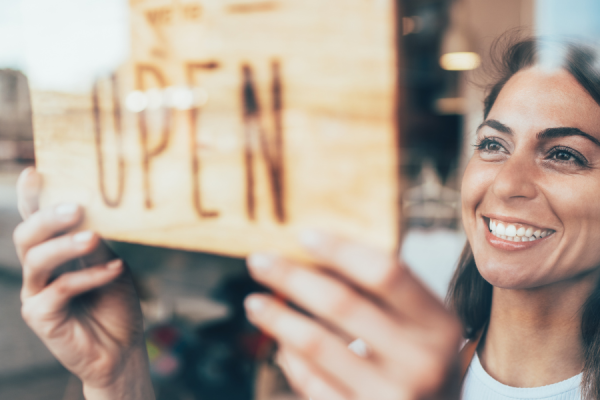 A woman turning around 'open' sign in the window
