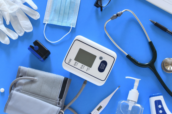 Medical equipment on a table: stethoscope, blood pressure reader, mask, clinical gloves, thermometer